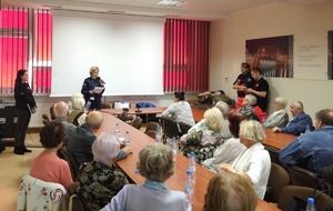 Policjanci i seniorzy podczas prelekcji. W tle prezentacja multimedialna.