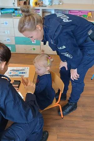 dwie policjantki pochylają się nad dziewczynką siedzącą na krzesełku