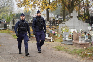 dwaj umundurowani policjanci patrolują pieszo teren cmentarza