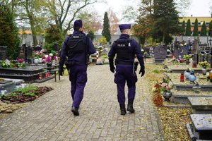 dwaj umundurowani policjanci patrolują pieszo teren cmentarza