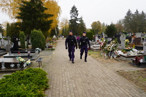dwaj umundurowani policjanci patrolują pieszo teren cmentarza