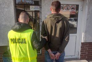 policjant trzyma zatrzymanego skutego kajdankami