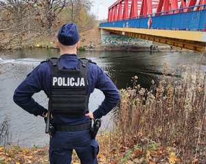 Policjant stoi na nabrzeżu rzeki.