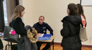 policjant siedząc przy biurku rozmawia z trzema studentkami
