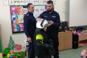 policjant zakłada chłopczykowi policyjny kask ochronny na głowę