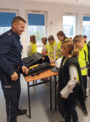 dziewczynka przymierza kamizelkę policyjną, przed nią stoi policjant, w tle inne dzieci