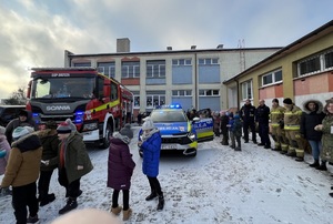 radiowóz i wóz strażacki przy szkole- obok policjanci i strażacy oraz kilkoro dzieci