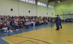 widok na siedzących na trybunach uczniów i przemawiających do nich policjantów