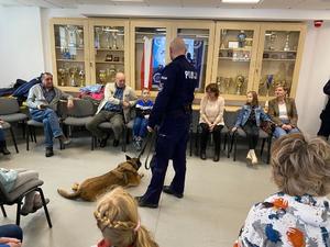 policjant wraz z psem służbowym, dookoła siedzą osoby, które się im przyglądają