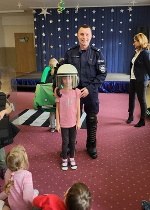 dziewczynka z policyjnym ochronnym kaskiem założonym na głowie stoi obok policjanta