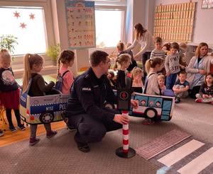 policjant i dzieci w sali przedszkola ćwiczą przy pomocy autochodzika