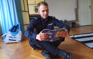 policjant siedząc na podłodze czyta dzieciom bajkę
