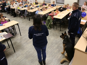 Uśmiechnięte dzieci słuchają prezentacji prowadzonej przez policjantów.