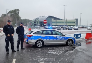 Policjanci wraz z radiowozem zabezpieczają dojazd do lotniska.