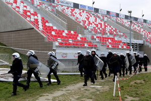 Policjanci biegną do działań z wyciągniętymi pałkami szturmowymi.