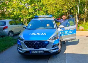 dziecko siedzi za kierownicą radiowozu, a przy nim stoi policjant