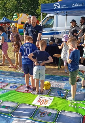 dzieci pod okiem policjanta grają na planszy edukacyjnej