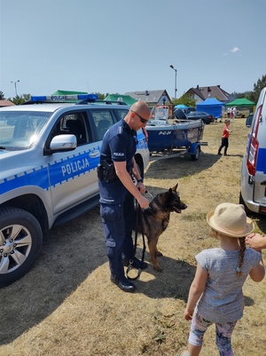 Policjant z psem rozmawia z dzieckiem, w tle policyjny sprzęt.