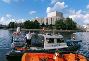 policjant stoi na zacumowanej łodzi motorowej na rzece, w tle Opera Nova
