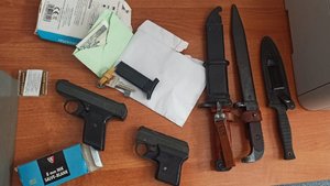 Broń, amunicja, pieniądze i noże leżące na stole