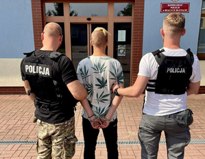 Policjanci trzymający osobę zatrzymaną przed komisariatem