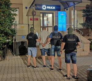 Policjanci stojący z zatrzymanym przed wejściem na komisariat