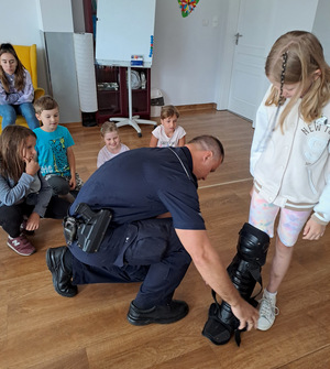 Policjant zakładający policyjne ochraniacze na nogi dziecku w przedszkolu