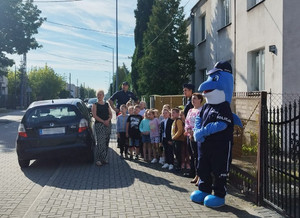 Uczniowie z policjantami i Polfinkiem podczas przechodzenia przez przejście dla pieszych.