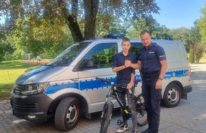 policjant i nastolatek z rowerem na tle policyjnego radiowozu