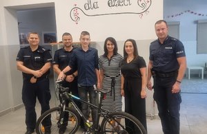 wspólne zdjęcie nastolatka z rowerem, opiekunów z placówki i policjantów