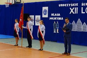 Ślubowanie uczniów klasy policyjnej i psychologiczno prawnej w szkole na sali gimnastycznej, gdzie uczestniczą w niej również zaproszeni goście oraz rodzice