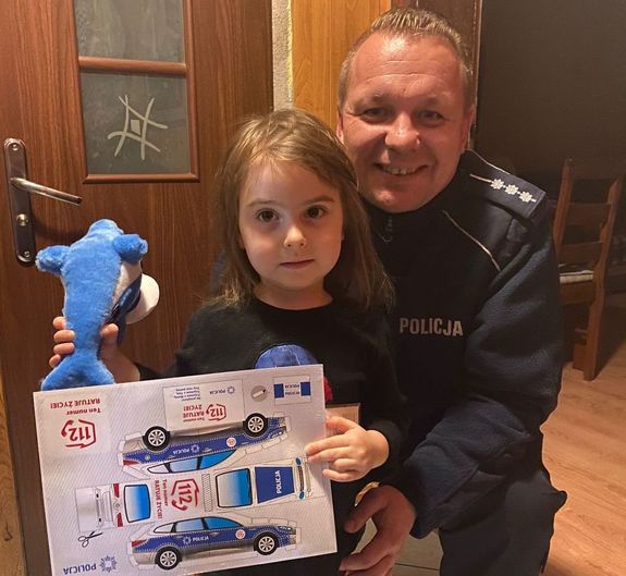 Policjant i 3-letnia Maja trzymająca prezenty.