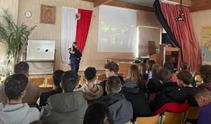 Policjanci i uczniowie podczas spotkania w auli szkoły. Wspólnie oglądają film promujący służbę w Policji.