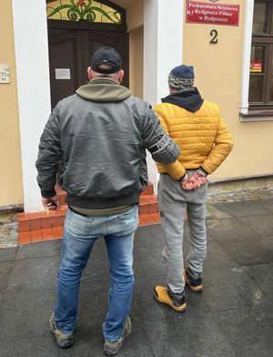 Policjant prowadzi zatrzymanego do budynku prokuratury.