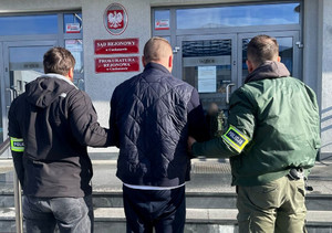 Policjanci prowadzą zatrzymanego do budynku sądu i prokuratury - zbliżenie.