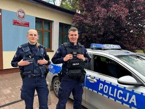 Patrol stojący przy radiowozie przed budynkiem komisariatu.
