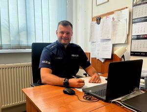 policjant stoi przy radiowozie przed komisariatem