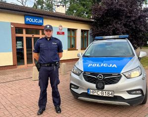 policjant stoi przy radiowozie przed komisariatem