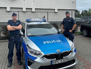 Dzielnicowi stojący przy radiowozie.