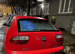 auto zaparkowane na ulicy, w tle stojące osoby i inne pojazdy oraz budynki