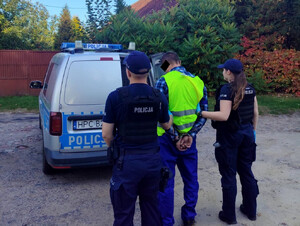 policjanci prowadzą zatrzymanego w stronę zaparkowanego radiowozu